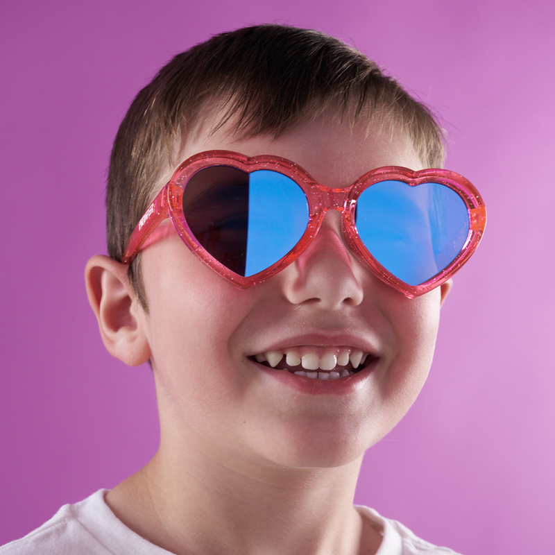 Blue-Purple | smile2.JPG | A smiling young boy wearing heart-shaped red sunglasses with blue mirrored lenses, set against a solid purple background.