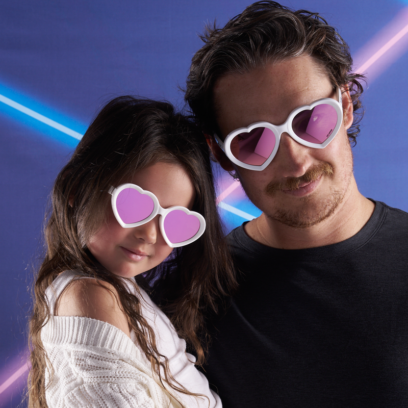 Pink | dad_can_also_match.JPG | A man and a young girl wearing white heart-shaped sunglasses with pink lenses, posed together against a blue background with neon light streaks.