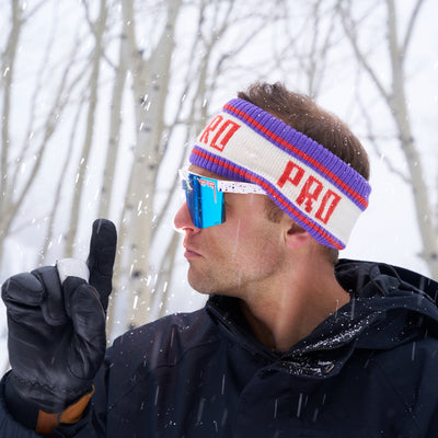 A man in a snowy place holding up one finger and wearing gloves, pit viper sunglasses and a pro half hat headband from Pit Viper. 