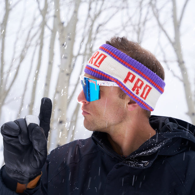 A man in a snowy place holding up one finger and wearing gloves, pit viper sunglasses and a pro half hat headband from Pit Viper. 