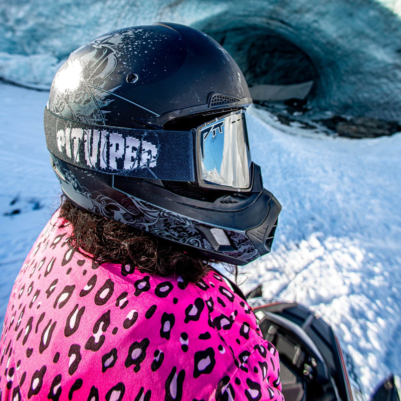 Silver | braaaap2.JPG | A person in a snowy outdoor setting wearing a black full-face helmet with a reflective visor and a bright pink leopard-print jacket, with an ice cave in the background.
