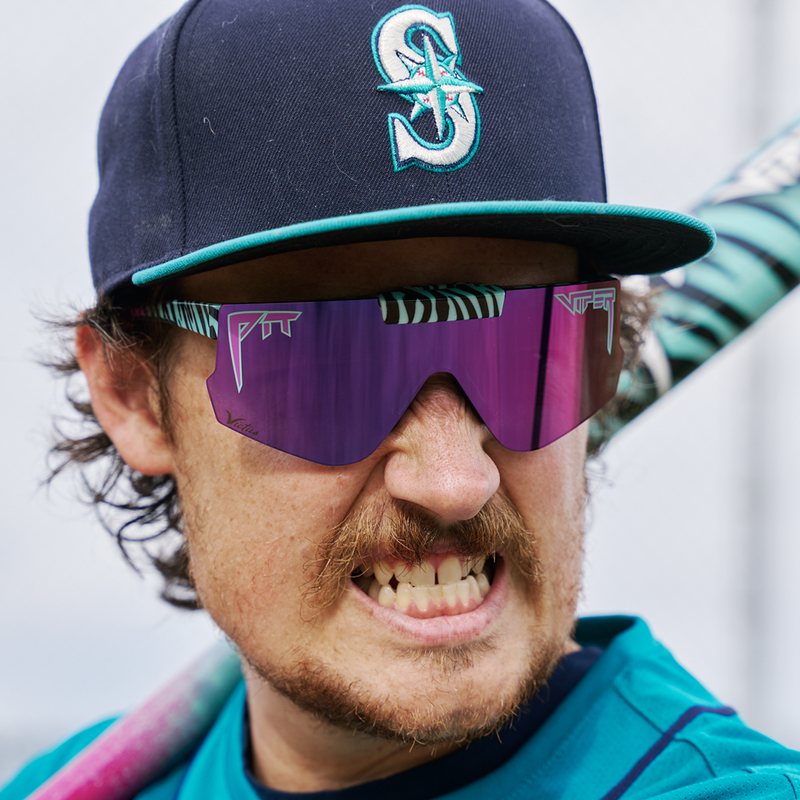 | player_photo.JPG | A close-up lifestyle shot of a man wearing a navy blue Seattle Mariners baseball cap and purple mirrored shield-style sunglasses with teal and white accents.