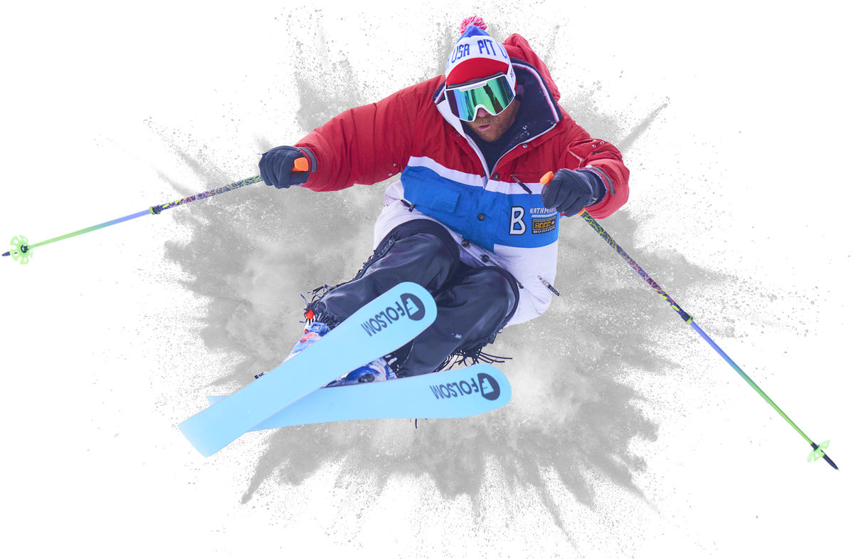 A skier in a red, white, and blue ski jacket with matching bib and goggles is captured mid-action against a white background with a gray spray effect. The skier is wearing light blue Rossignol skis and holding ski poles.