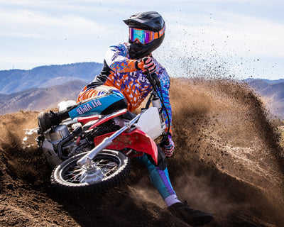 Person riding a dirt bike on a dirt track with mountains in the background